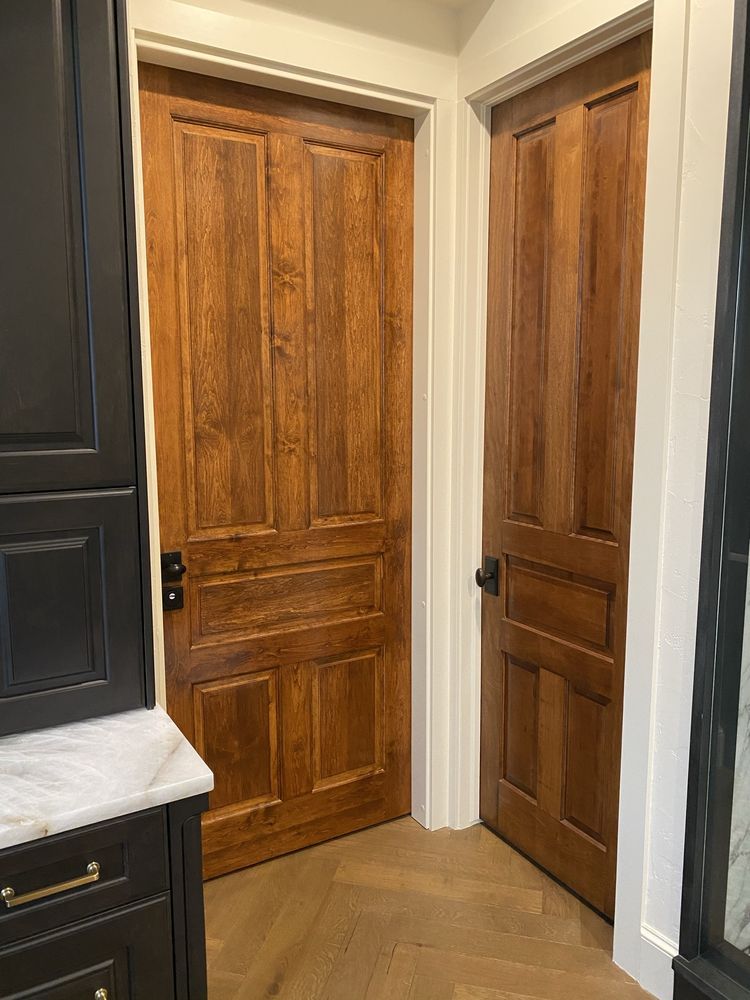 Two wooden doors with dark hardware, brown cabinets, and a marble countertop.