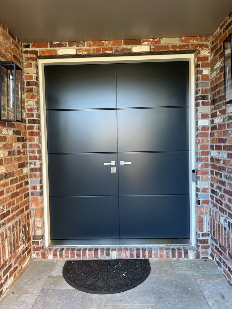 Black double front doors with silver handles, set in a brick and white trim doorway, with a black doormat.