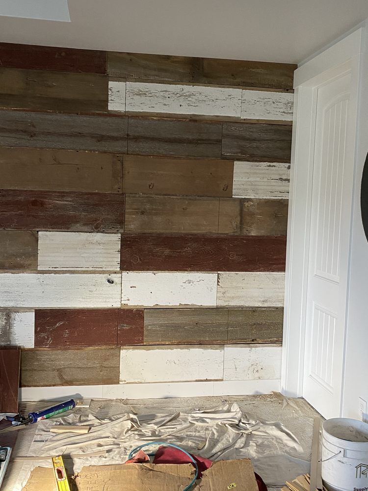 A partially finished accent wall with multicolored wood planks, adjacent to a white door.