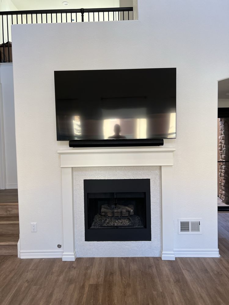 TV and soundbar mounted above a fireplace, set in a white wall.