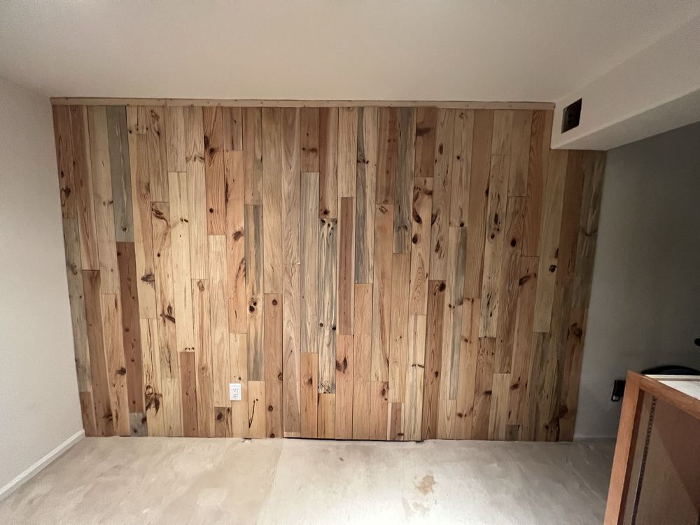 Wooden plank accent wall in a room, with a light-colored floor and white walls.