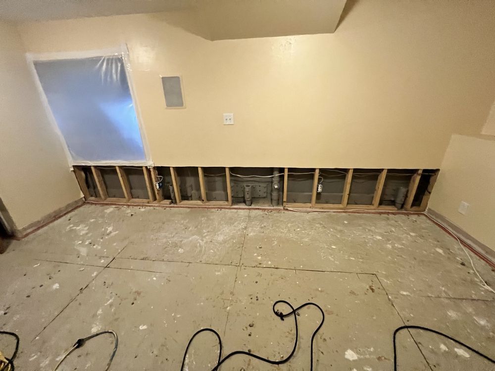 Room renovation with exposed wall studs, and floor debris. Beige walls and gray floor.