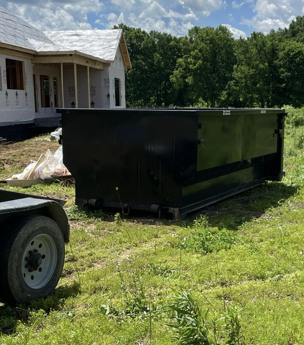 A green dumpster filled with wood is sitting in the grass.