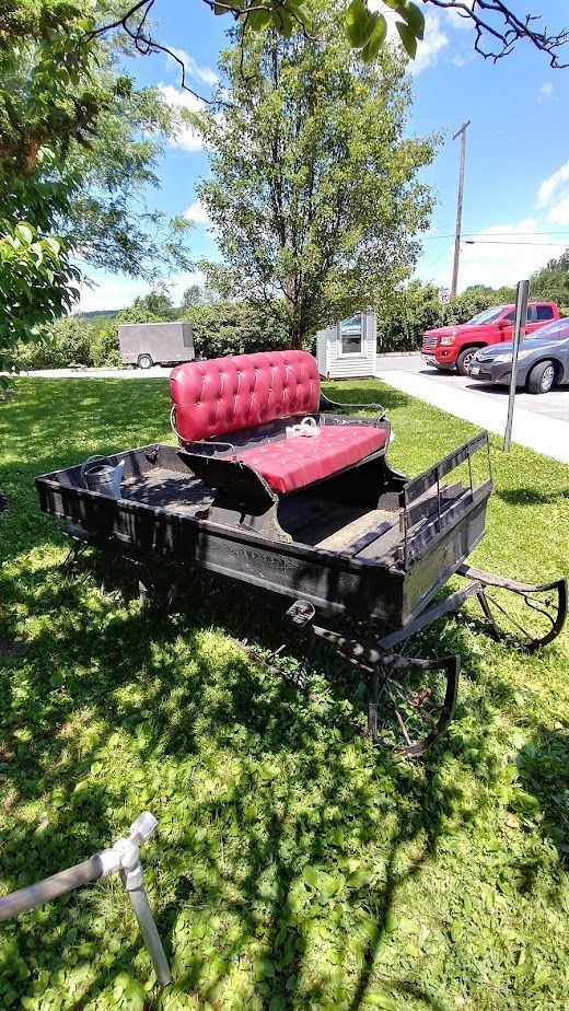 A horse drawn carriage with a red seat is parked in the grass.