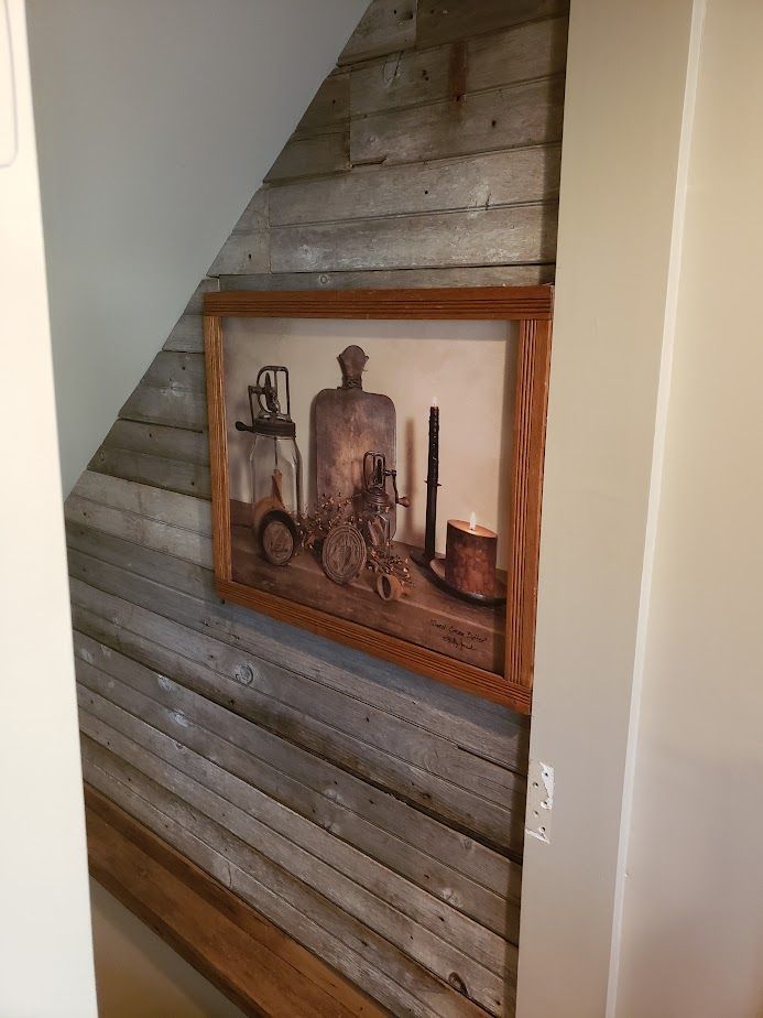 A framed picture on a wooden wall under a staircase