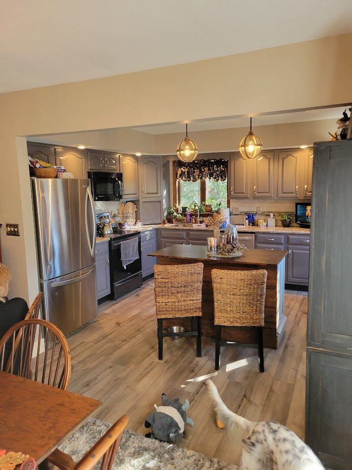 A kitchen with stainless steel appliances , wicker chairs , a table and a dog laying on the floor.