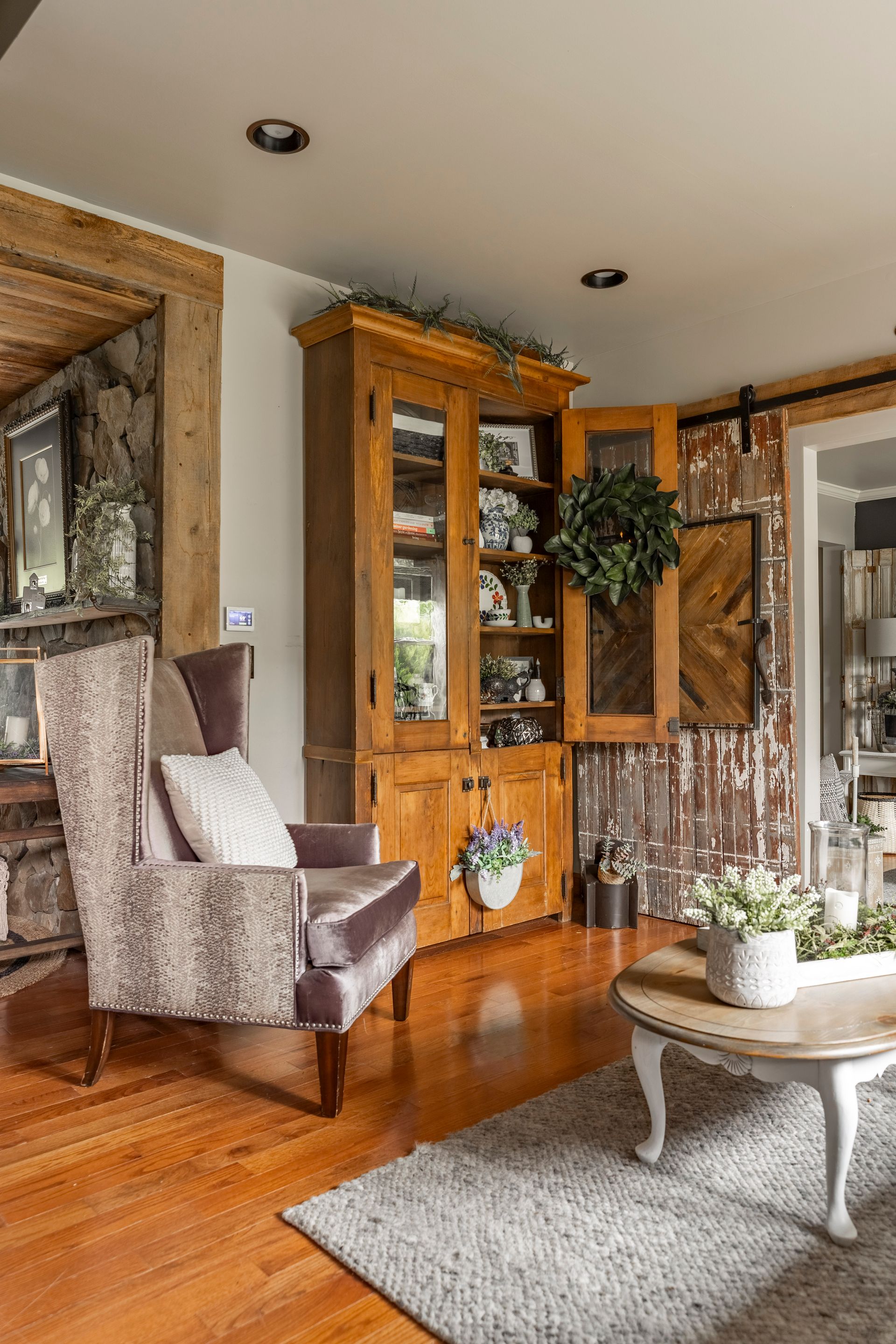 A living room with hardwood floors , a chair , a coffee table and a hutch.