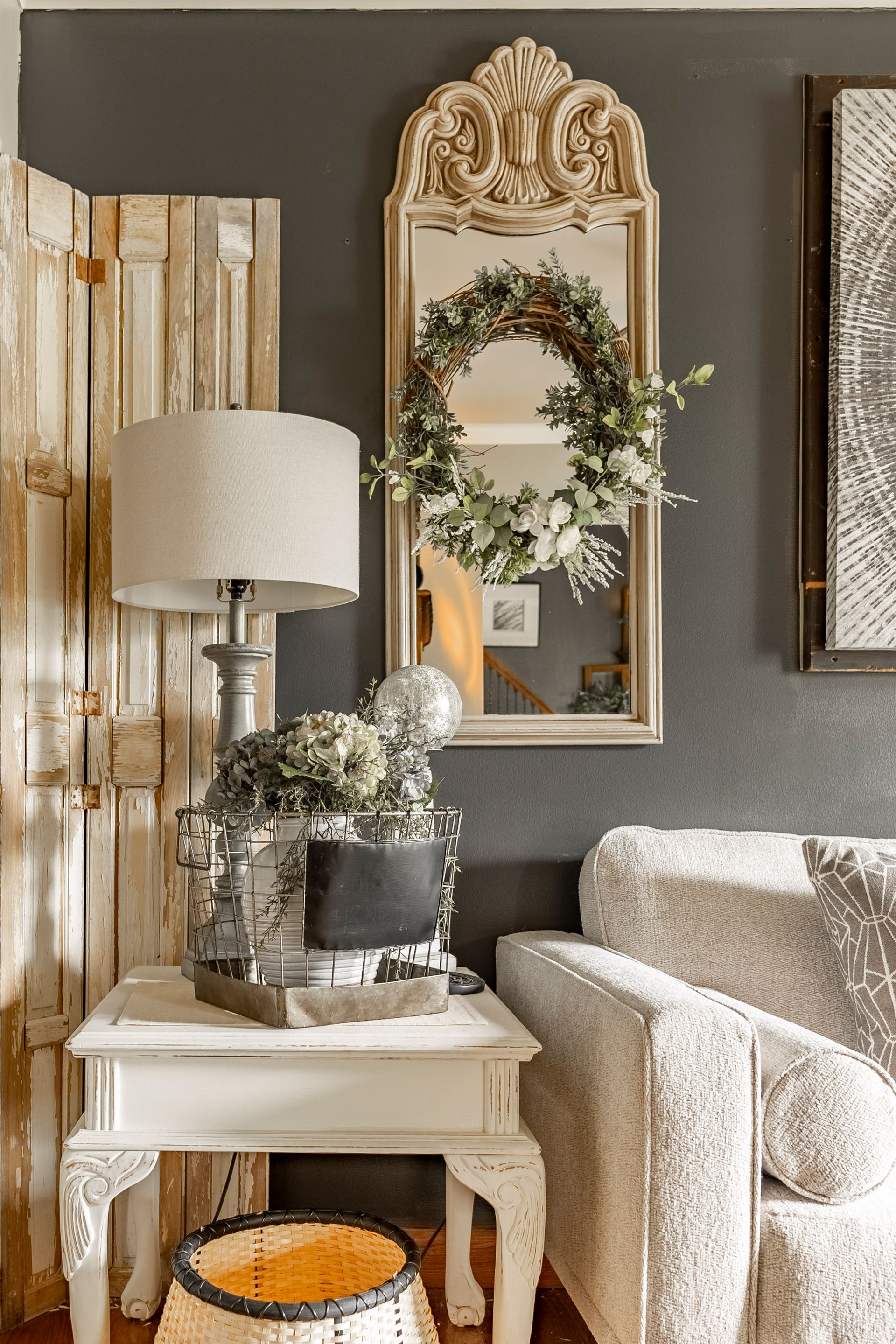 A living room with a couch , chair , table , lamp and mirror.