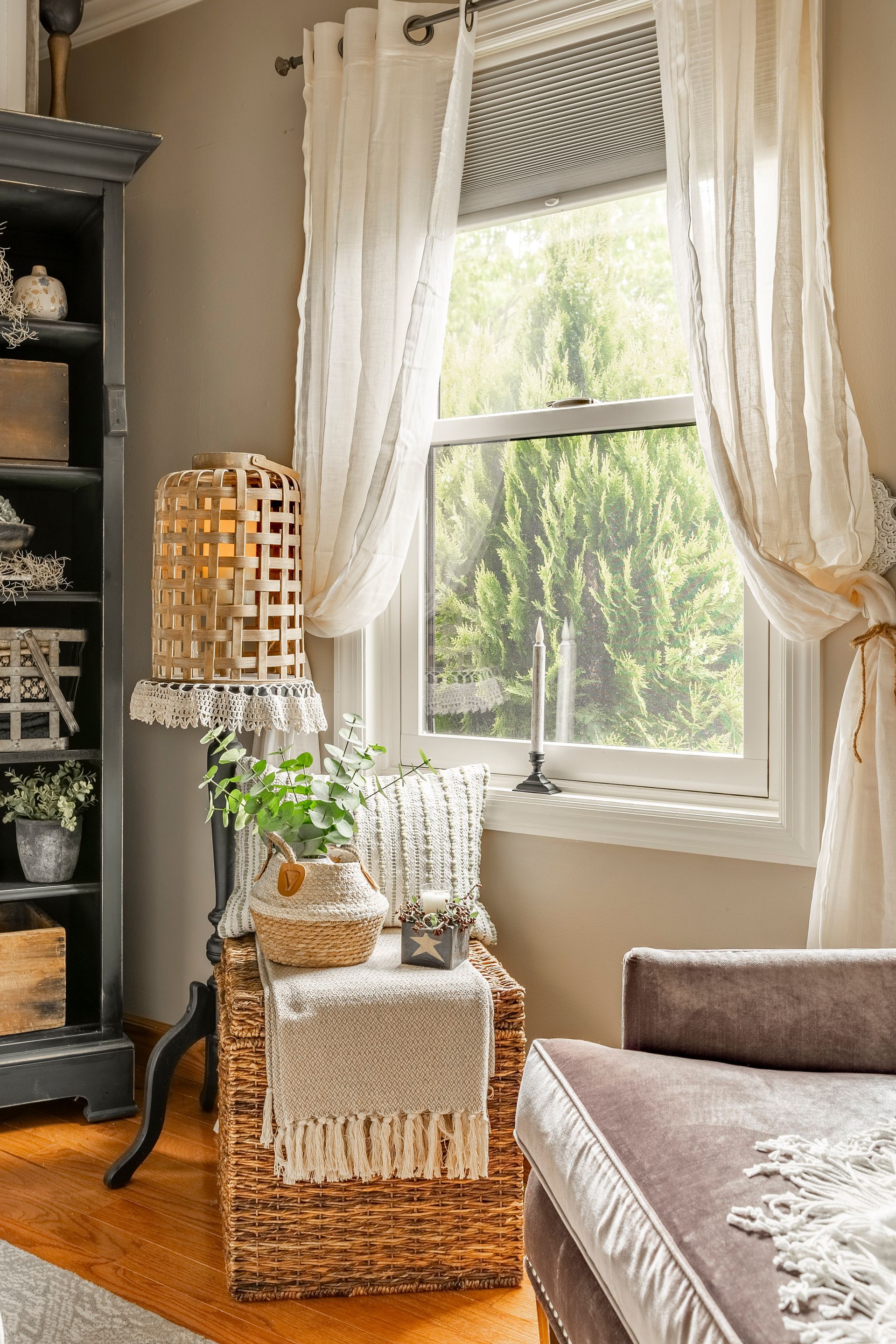 A living room with a wicker chair , couch , bookshelf and window.