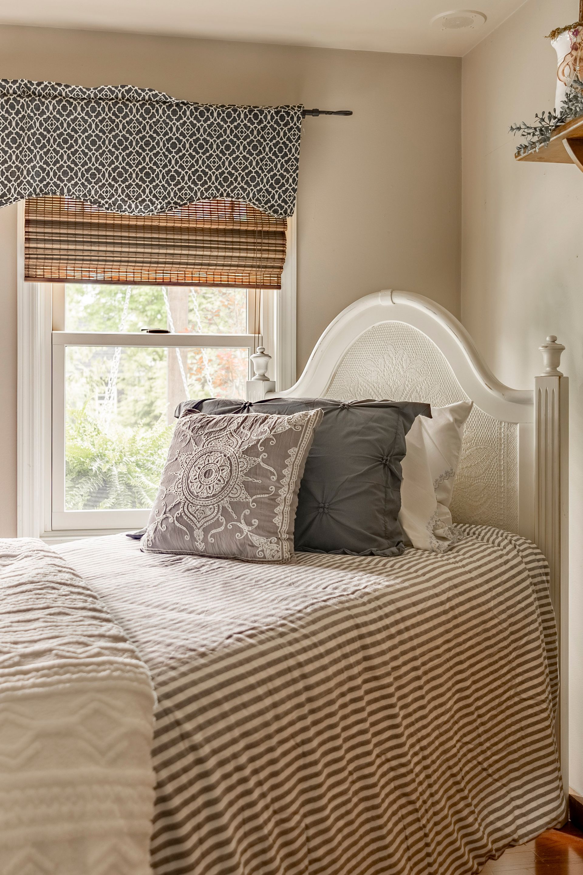 A bed with a striped comforter and pillows in a bedroom next to a window.
