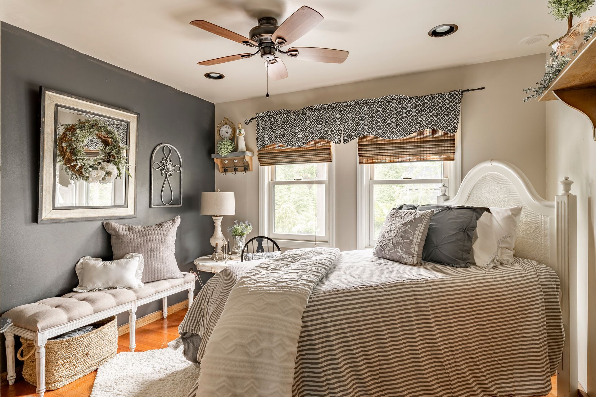 A bedroom with a bed , bench , ceiling fan and two windows.