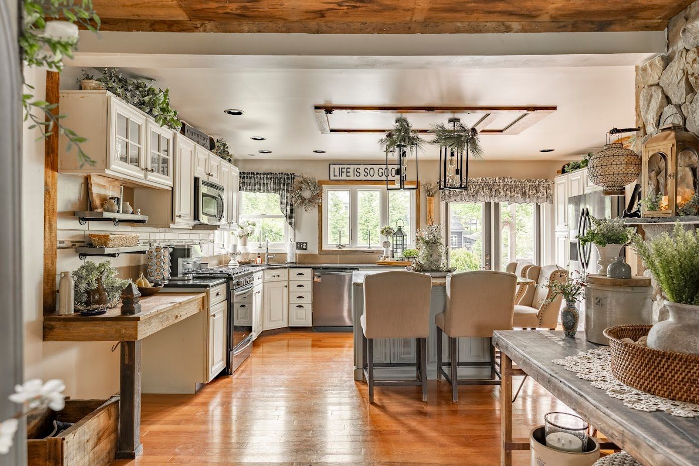 A kitchen with white cabinets , stainless steel appliances , hardwood floors and a wooden ceiling.