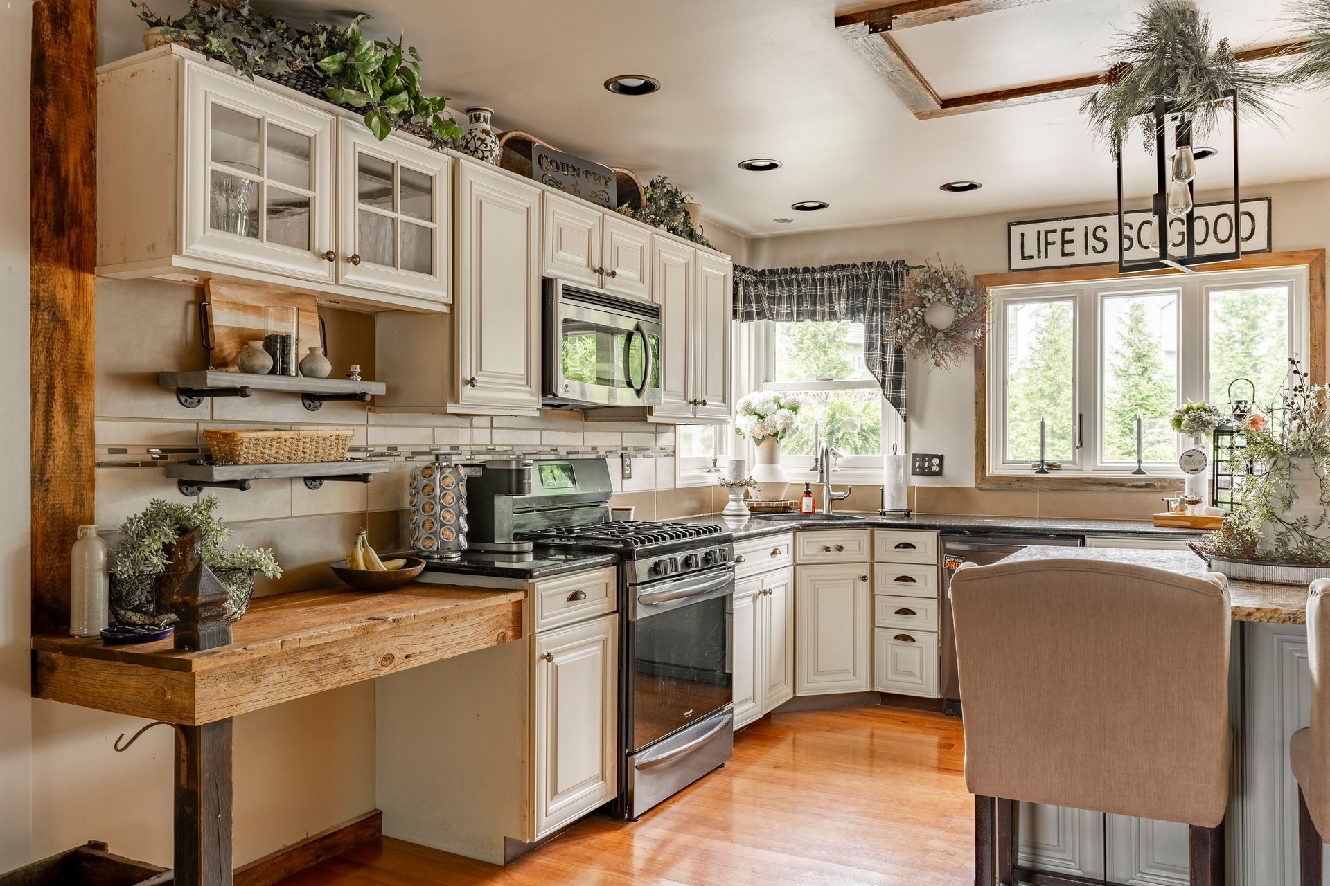A kitchen with white cabinets , a stove , a microwave , and a wooden table.
