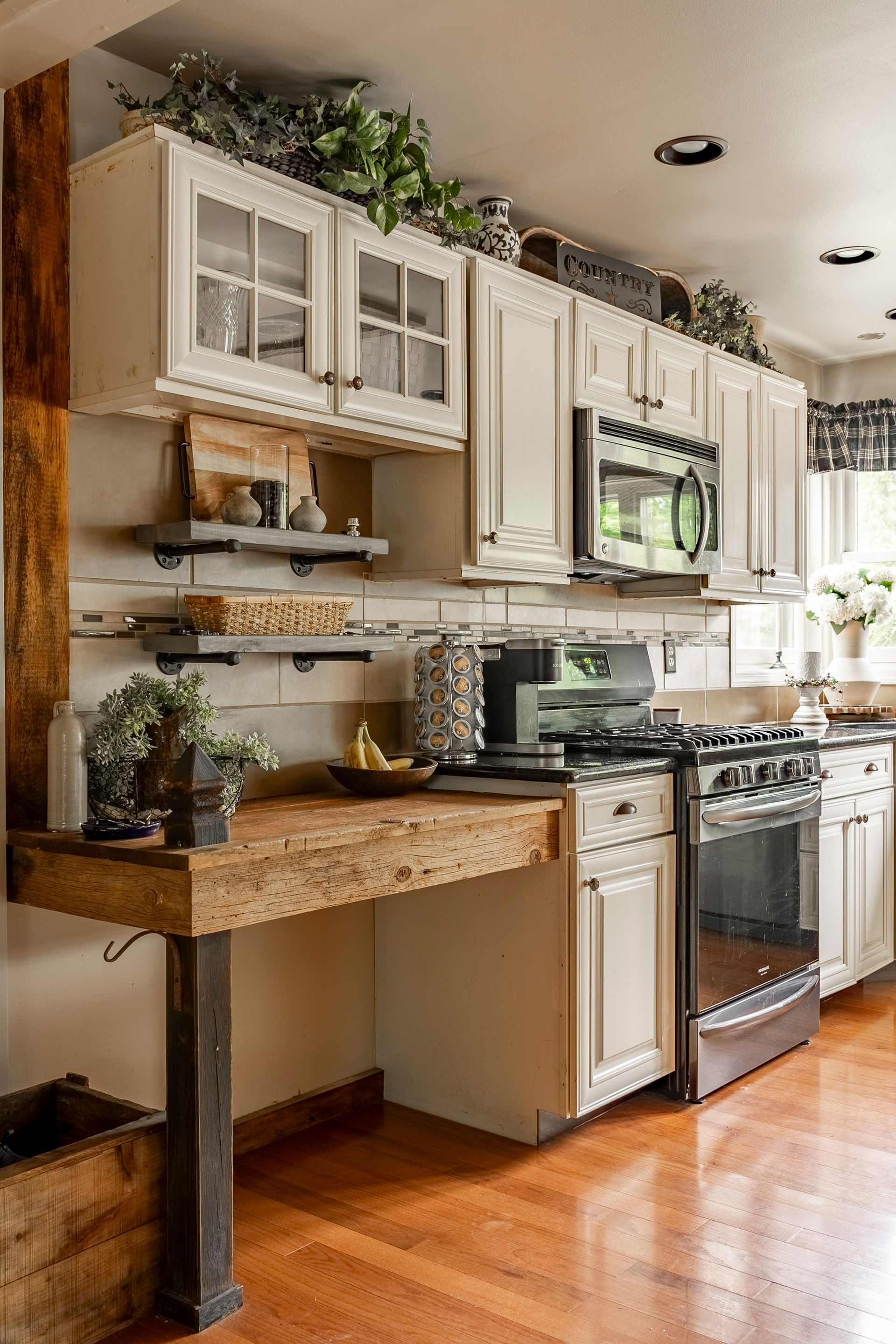 A kitchen with white cabinets , a stove , a microwave , and a wooden counter.