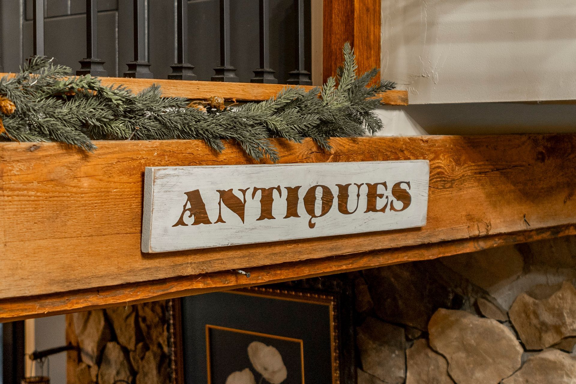 A wooden sign that says antiques is on a wooden mantle.