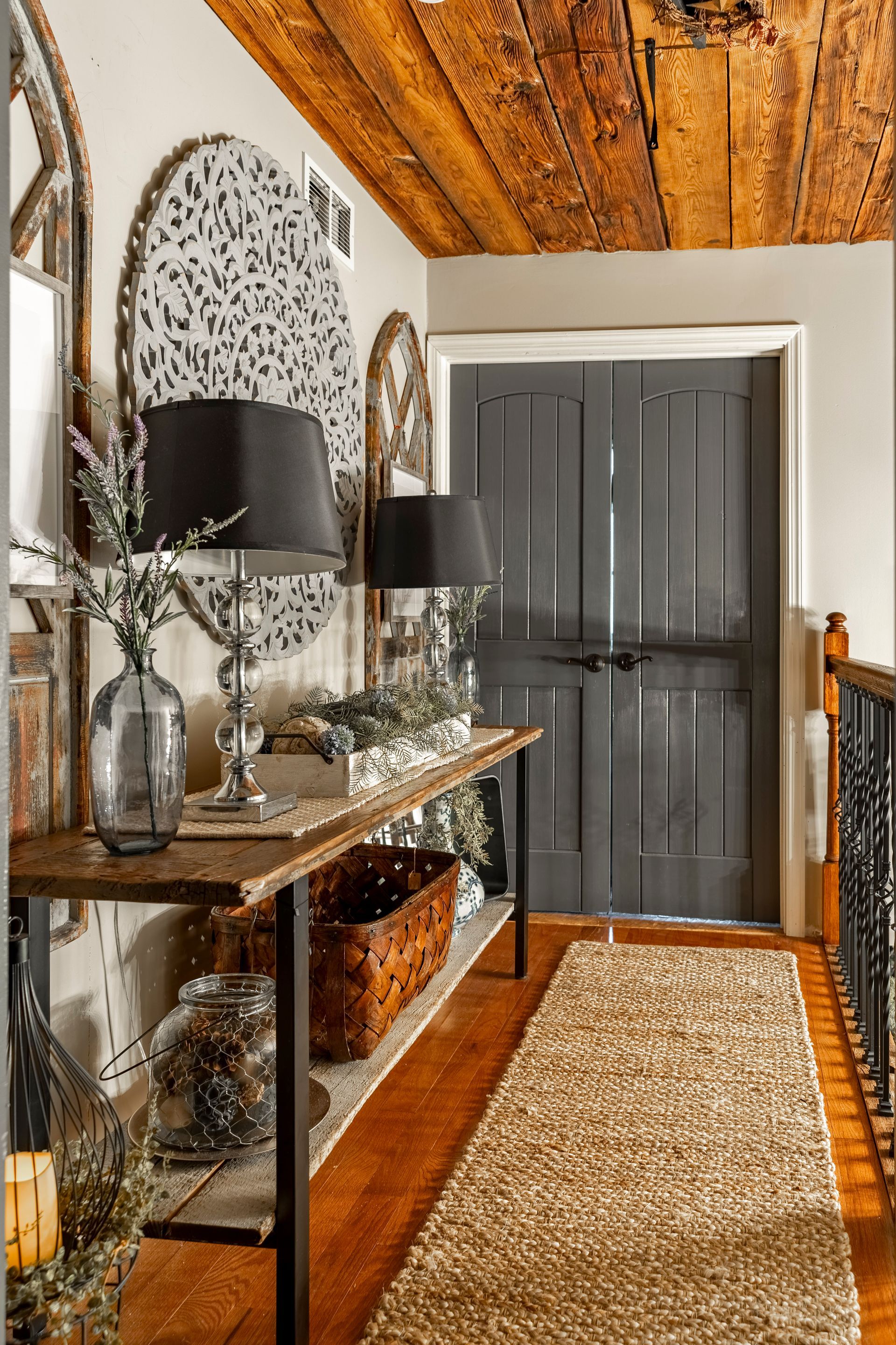 A hallway with a wooden ceiling , a table , lamps , and a rug.