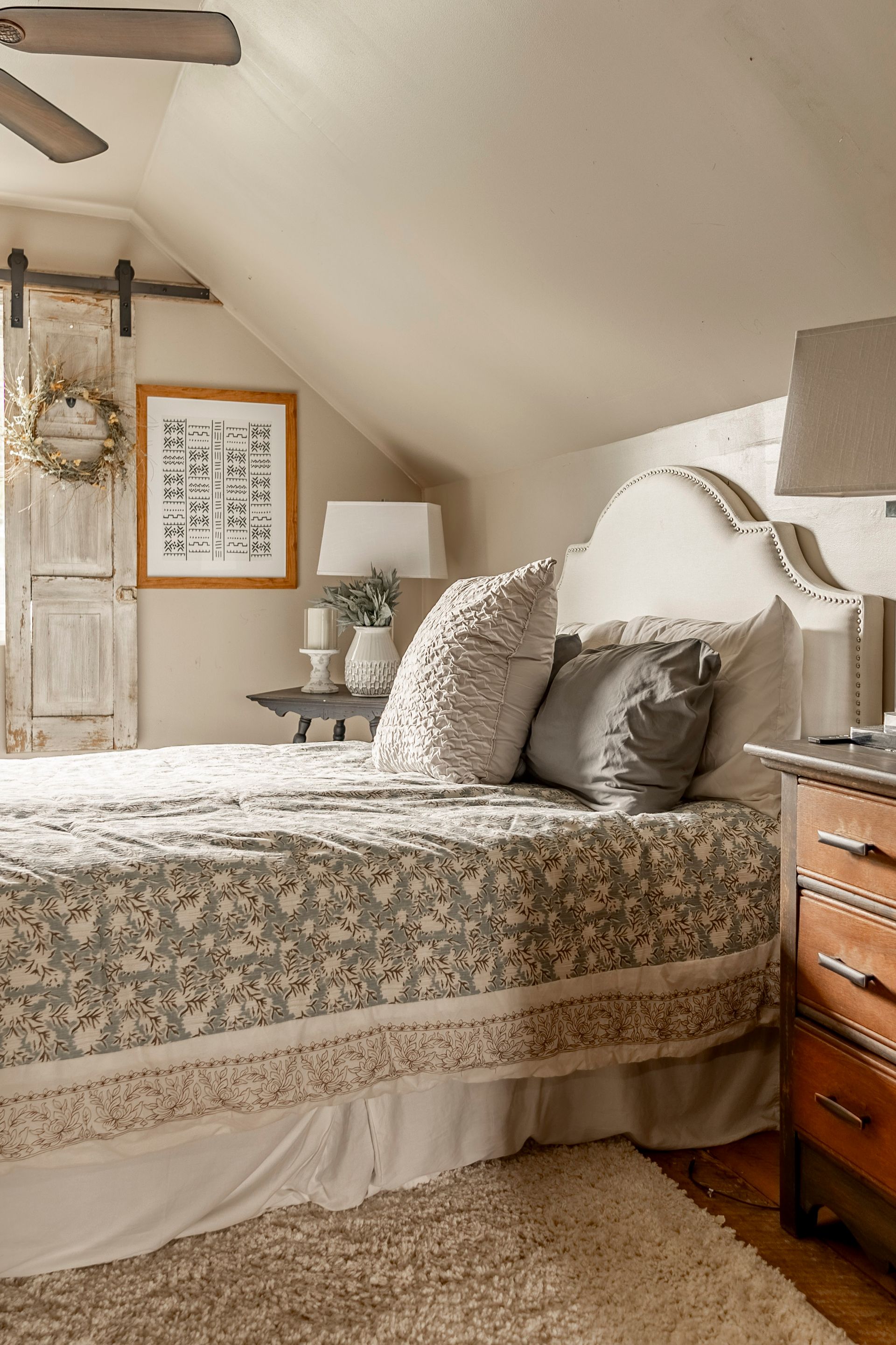 A bedroom with a bed , nightstand , lamp and sliding barn door.