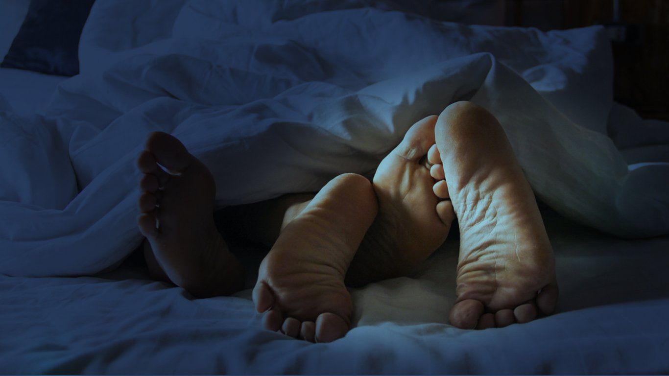 A couple 's feet are sticking out of the blankets on a bed.
