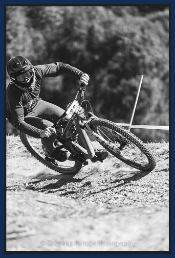 A black and white photo of a person riding a bike on a dirt road.