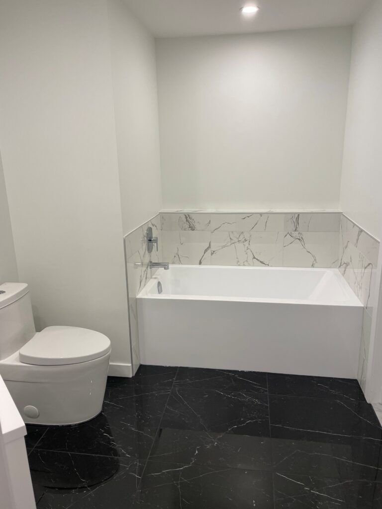 Salle de bains blanche avec sol carrelé noir ; toilettes et baignoire avec crédence en marbre.