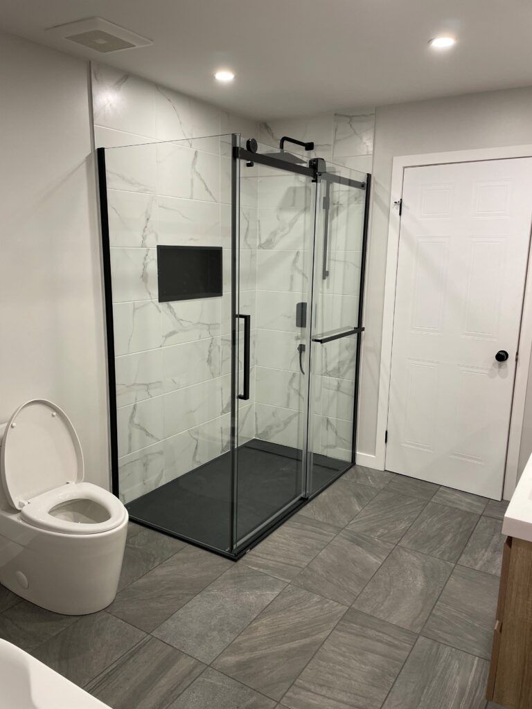 Salle de bains moderne avec cabine de douche en verre, toilettes et sol carrelé gris.