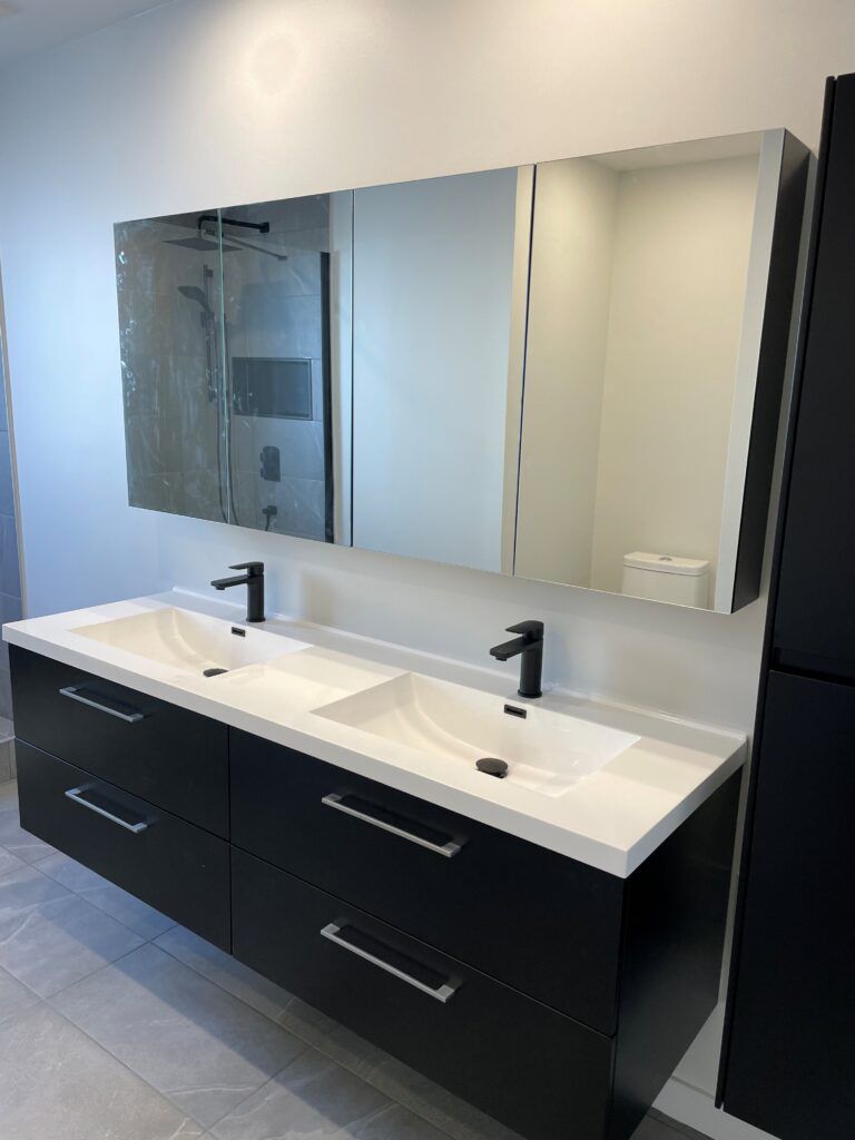 Salle de bains moderne avec double vasque noire, comptoir blanc, robinetterie noire et grand miroir.