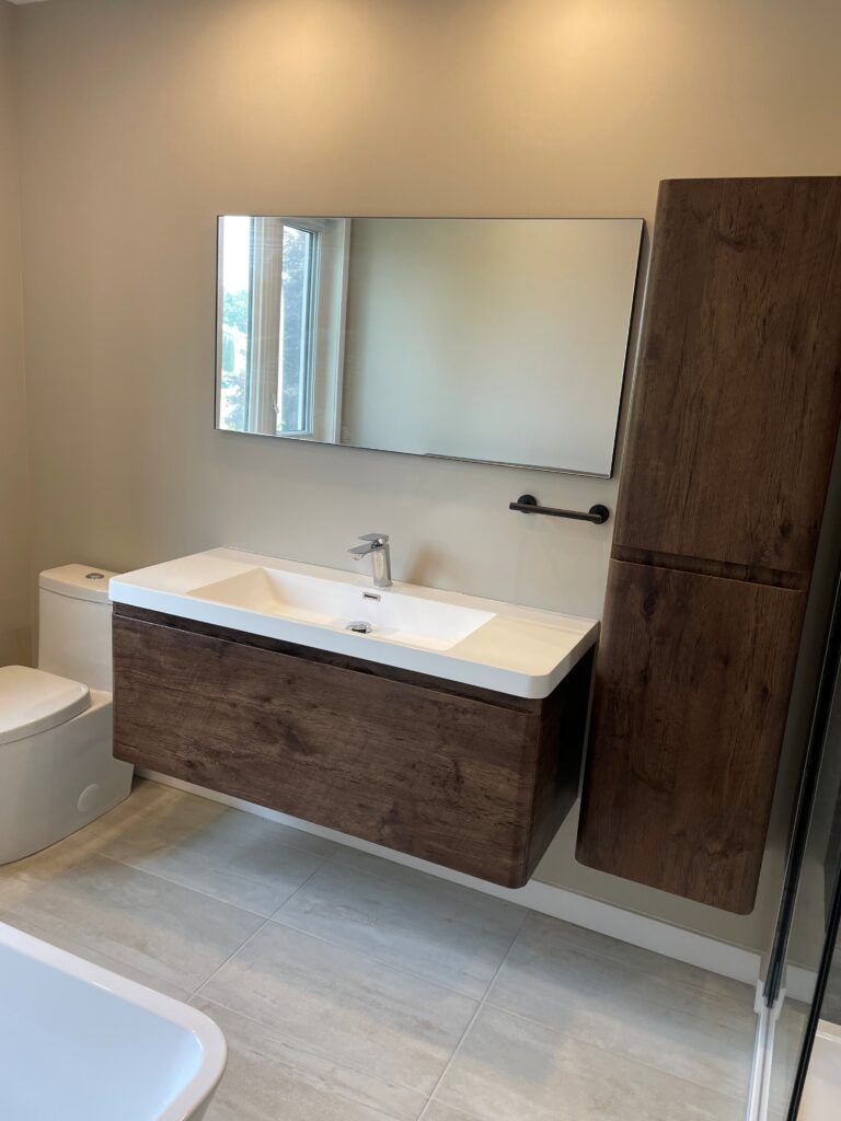 Salle de bains moderne avec meuble-lavabo suspendu en bois, grand miroir et armoire de rangement haute.