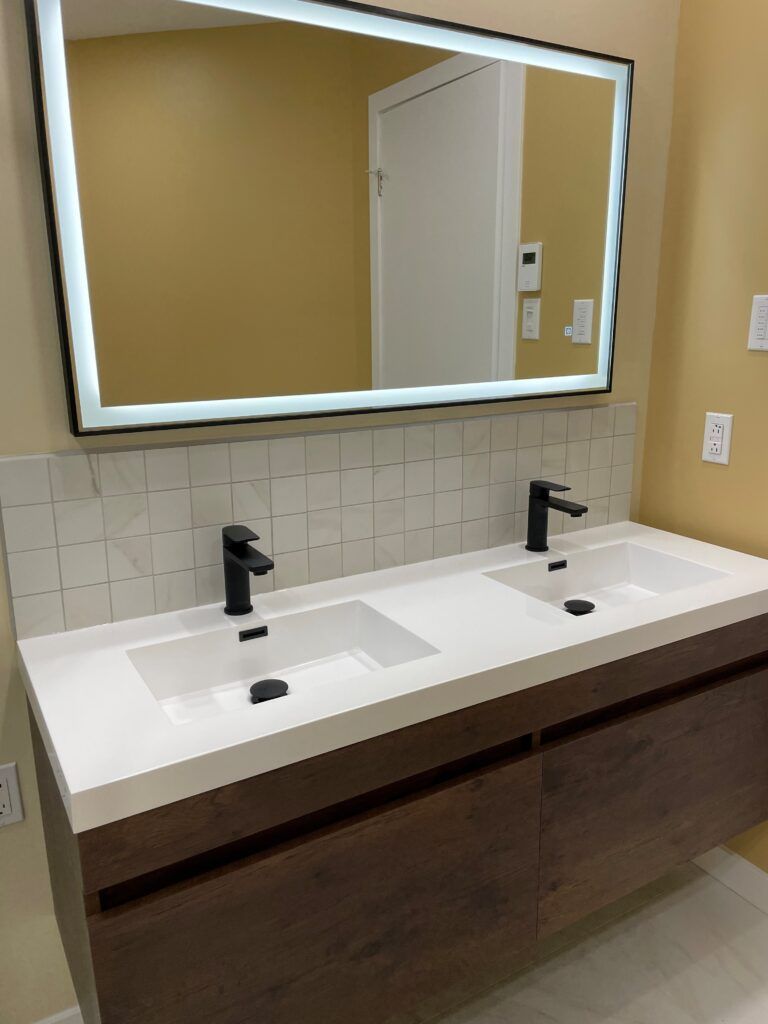 Salle de bains moderne avec double vasque, robinetterie noire et miroir rétroéclairé au-dessus d'un meuble-lavabo suspendu en bois.