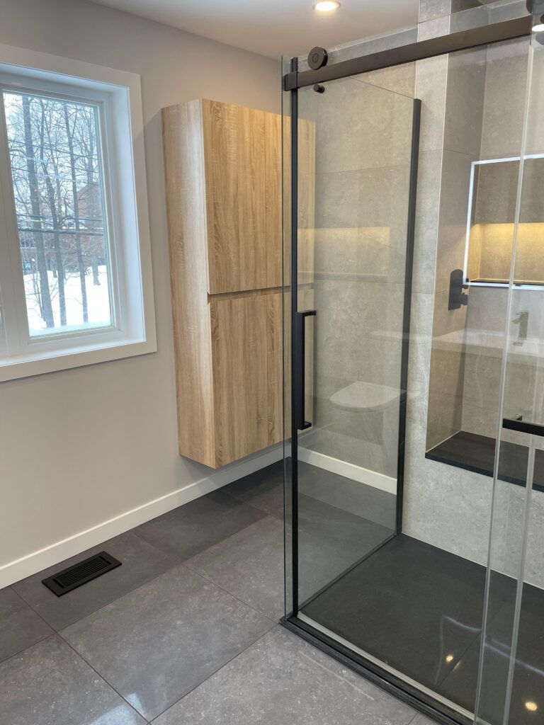 Salle de bains moderne avec meuble en bois, douche en verre et sol carrelé gris.
