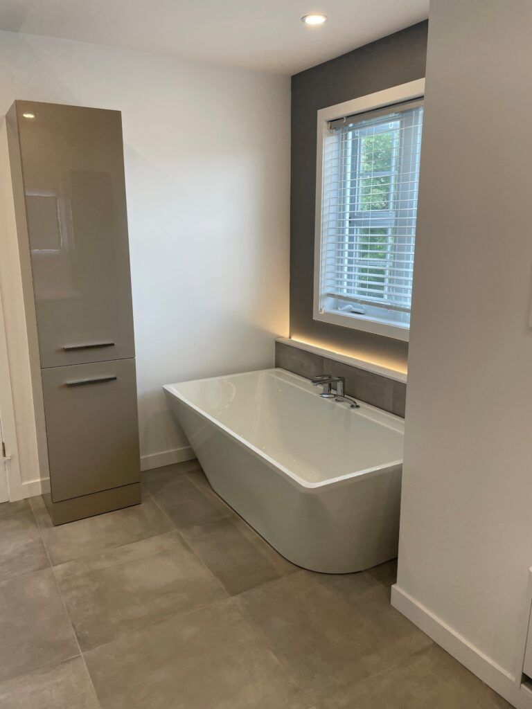 Salle de bains moderne avec baignoire îlot, meuble de rangement et fenêtre avec stores.