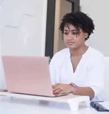 Femme travaillant sur un ordinateur portable rose doré dans un bureau lumineux.