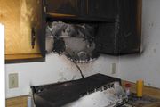 Burned kitchen stove and cabinets with fire damage and soot on the wall