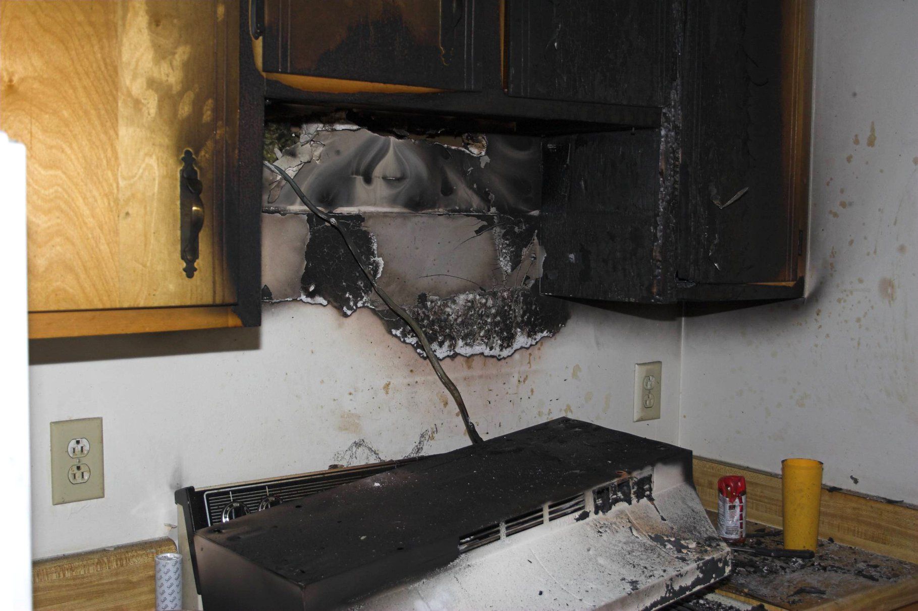 Burned kitchen stove and cabinets with fire damage and soot on the wall