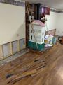 Partially stripped room with exposed walls, wood floor, and a child’s toy house and ladder in the corner