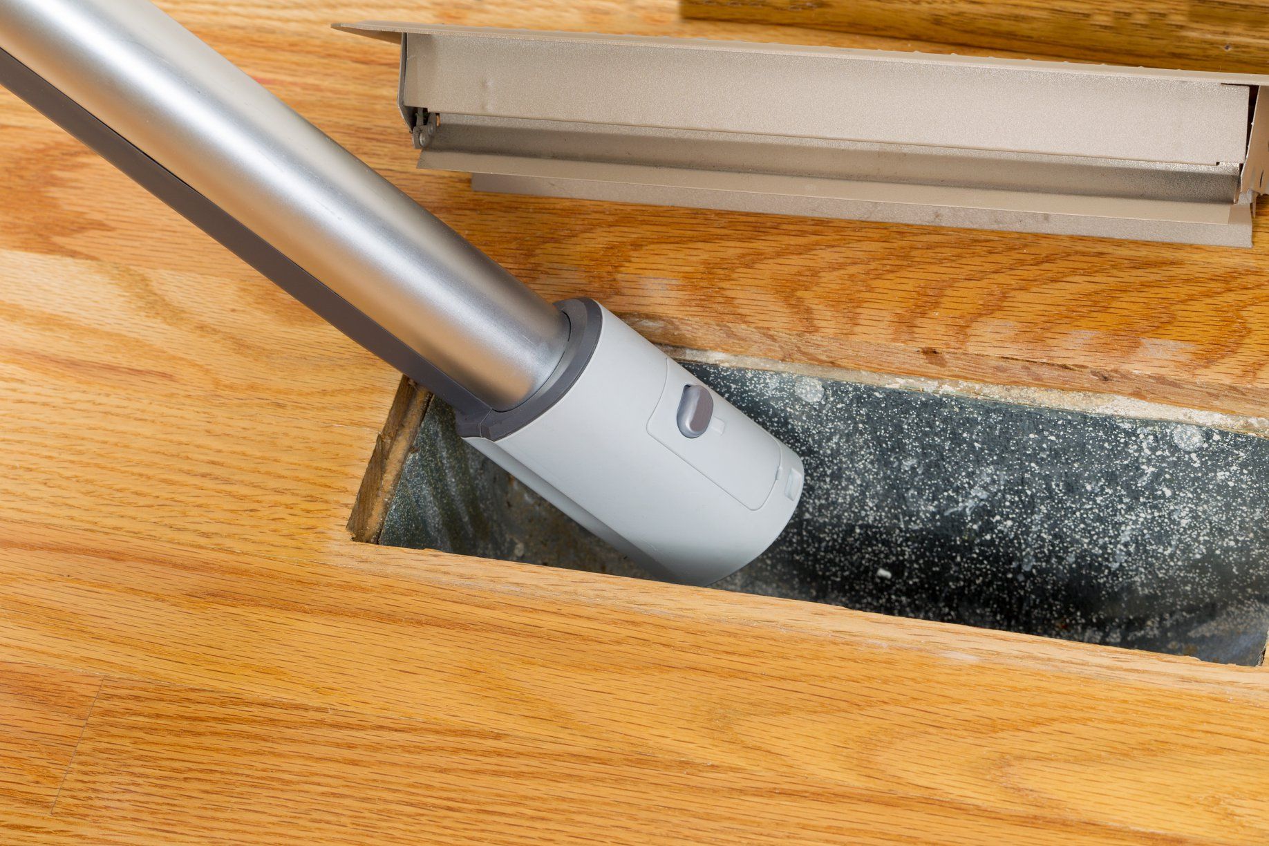 Vacuum cleaner head on a wooden floor, cleaning a dark carpet strip
