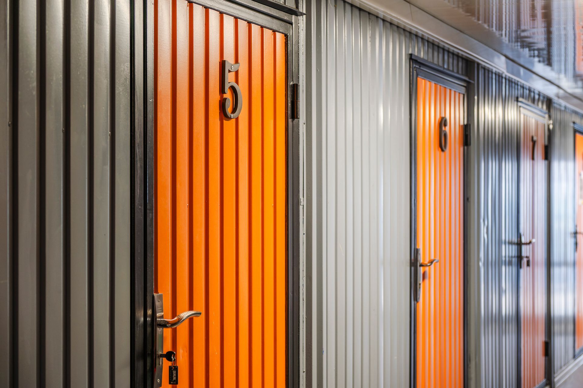 Row of storage unit doors, some orange and some gray, each with a number.