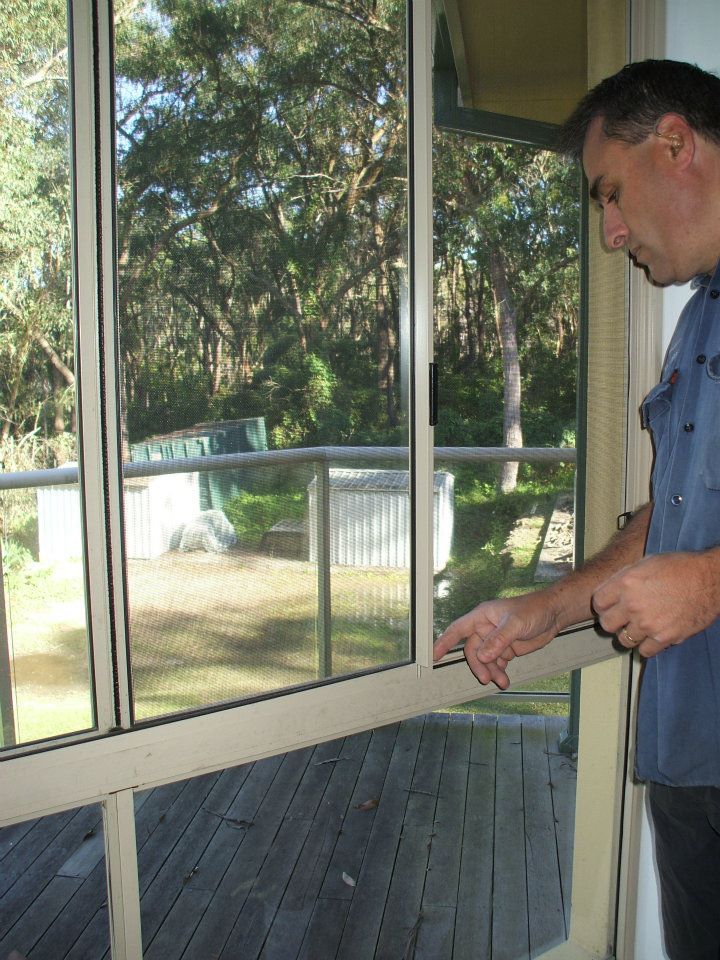 Man Points at a Sliding Glass Window Overlooking a Backyard With Trees and a Deck — Fix-A-Door in Morisset, NSW