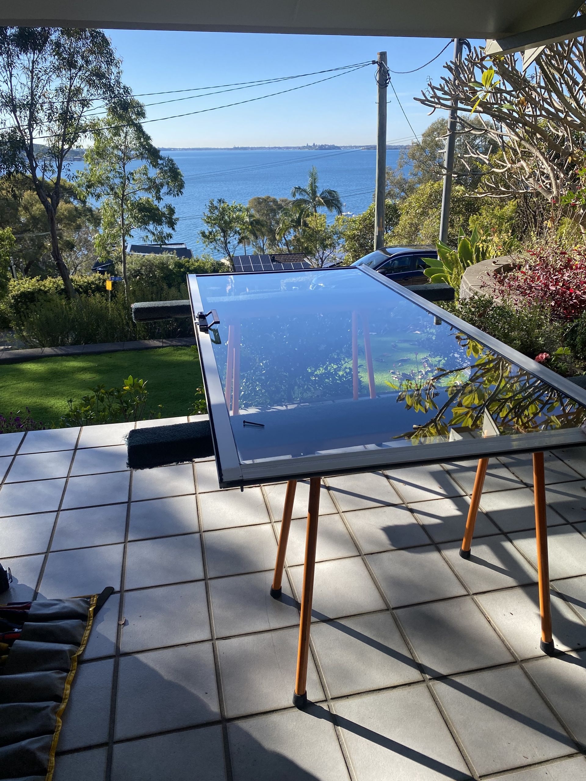 Large glass pane on a sawhorse on a patio overlooking a bay and trees on a sunny day— Fix-A-Door in Morisset, NSW