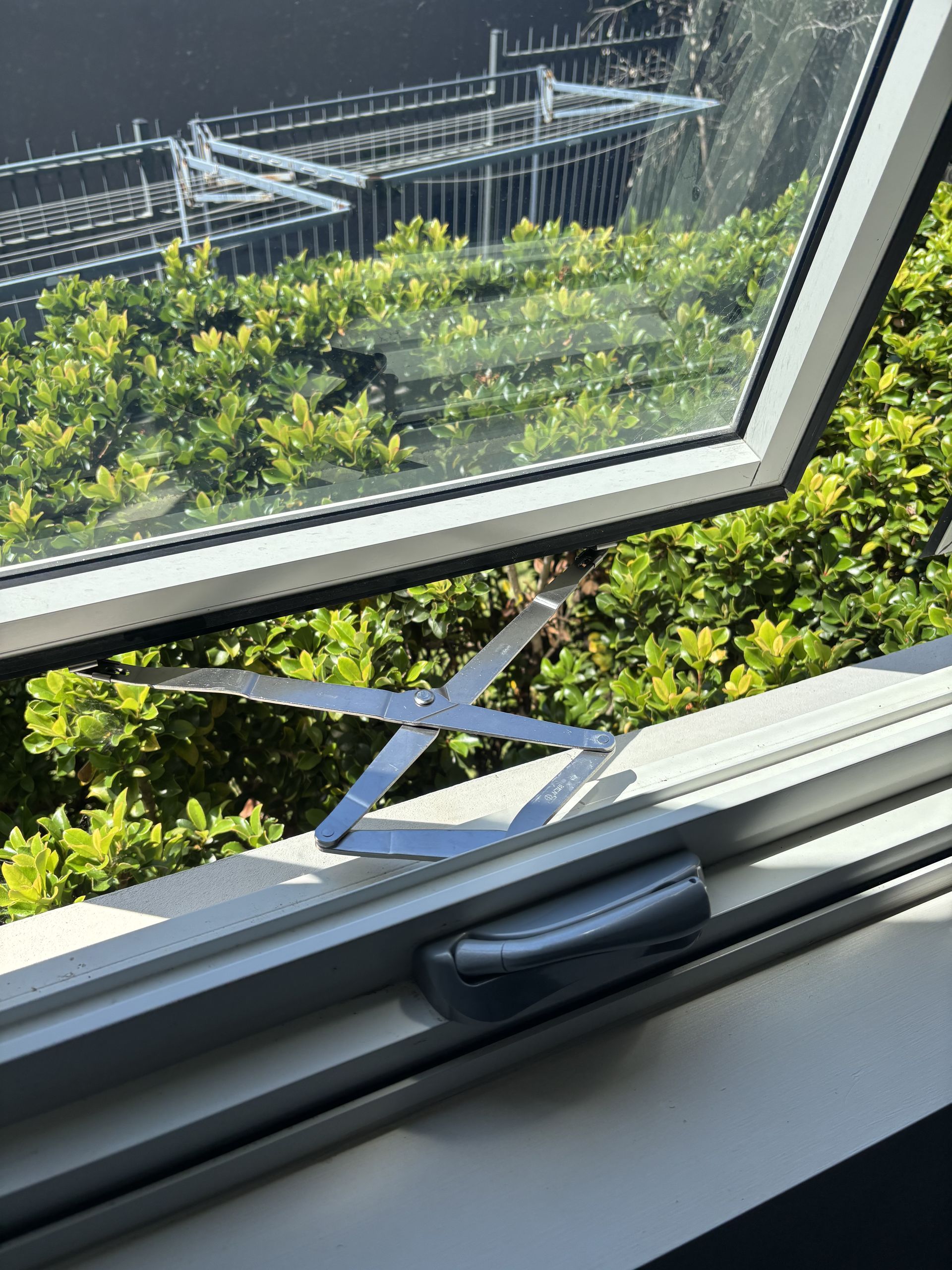 Open window with metal arms, overlooking green bushes and a distant structure-Fix-A-Door in Morisset, NSW