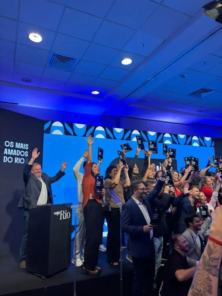 A group of people standing on a stage at an awards ceremony, holding plaques and cheering under blue stage lighting.