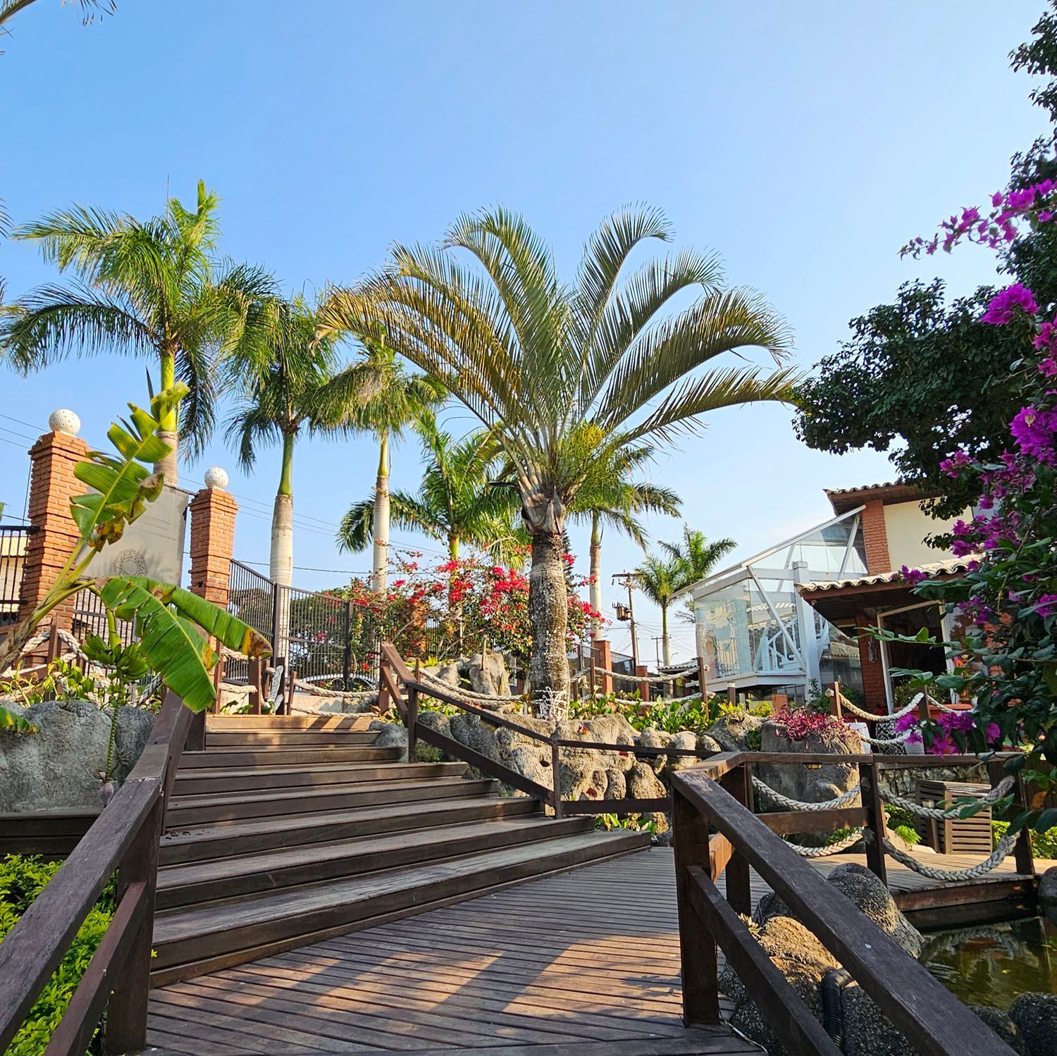 Uma ponte de madeira que leva a um edifício com palmeiras ao fundo