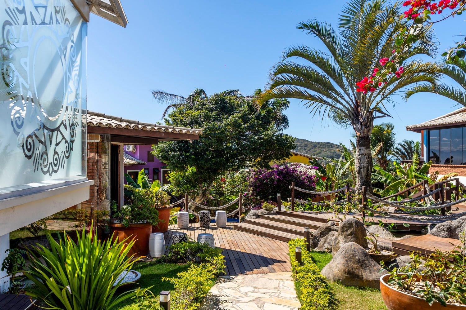 Um jardim verdejante com palmeiras e flores em frente a uma casa.