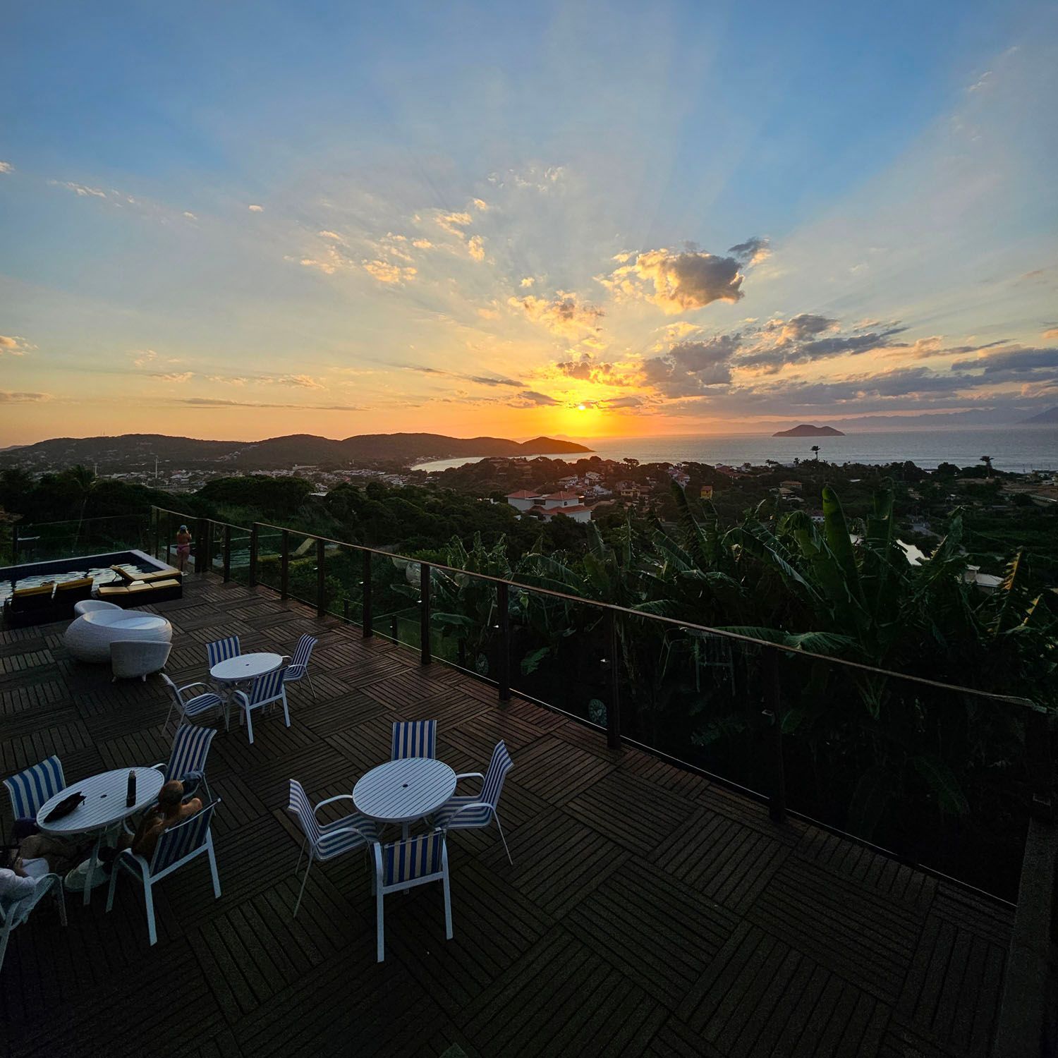 Um pôr do sol sobre um deck de madeira com mesas e cadeiras