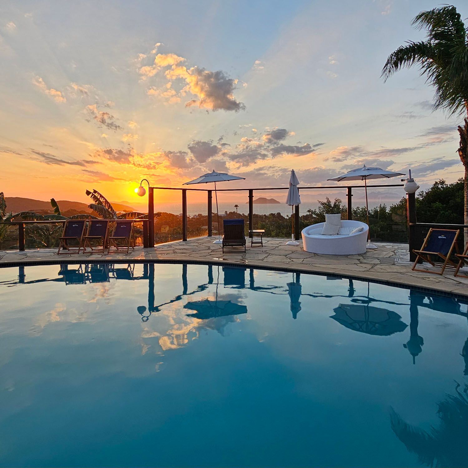 Uma grande piscina com cadeiras e guarda-sóis ao redor ao pôr do sol
