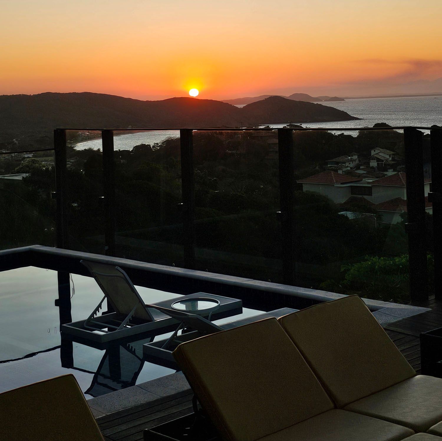 Um pôr do sol sobre um corpo de água com uma piscina em primeiro plano