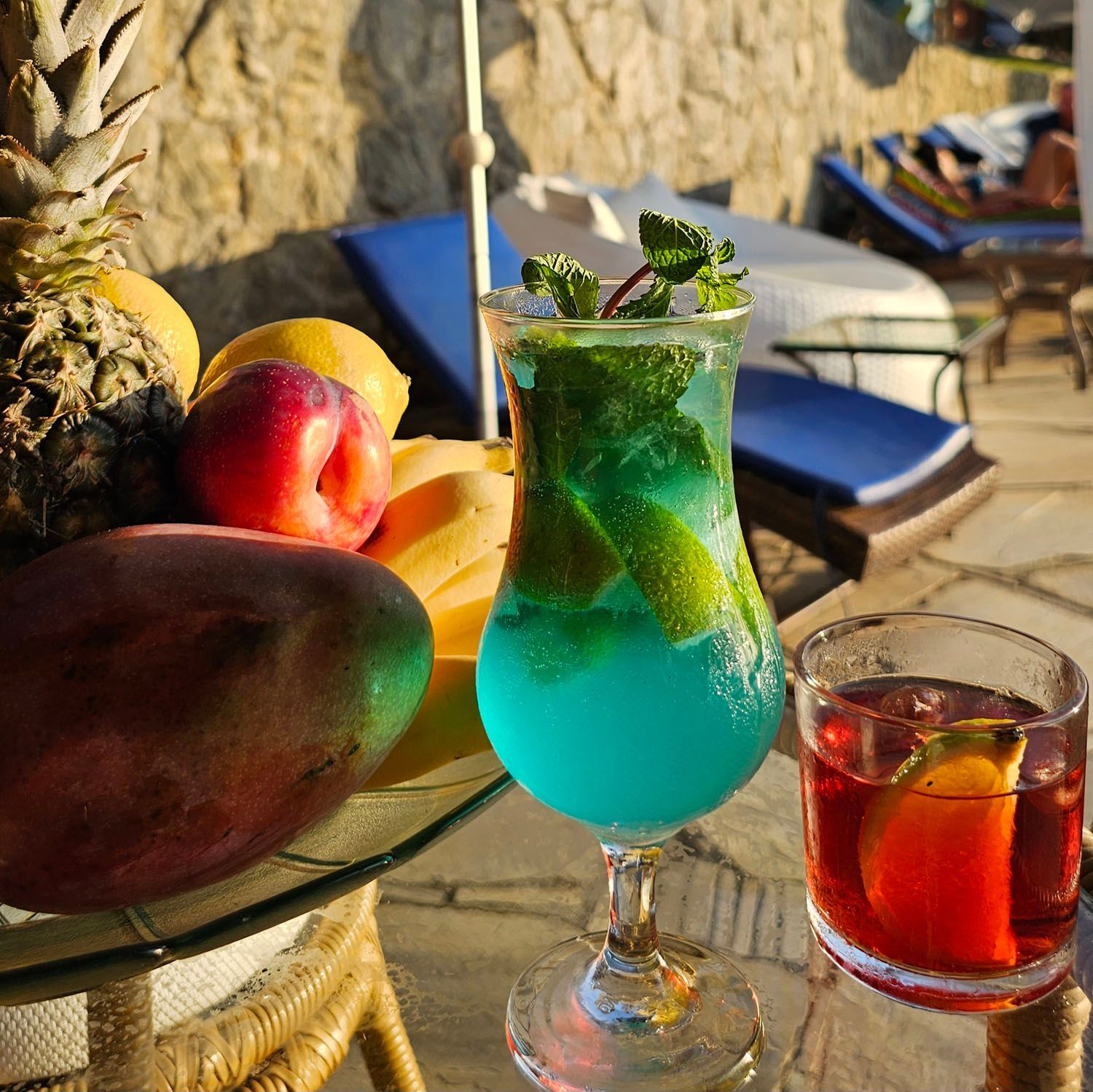 Uma bebida azul em um copo ao lado de uma tigela de frutas