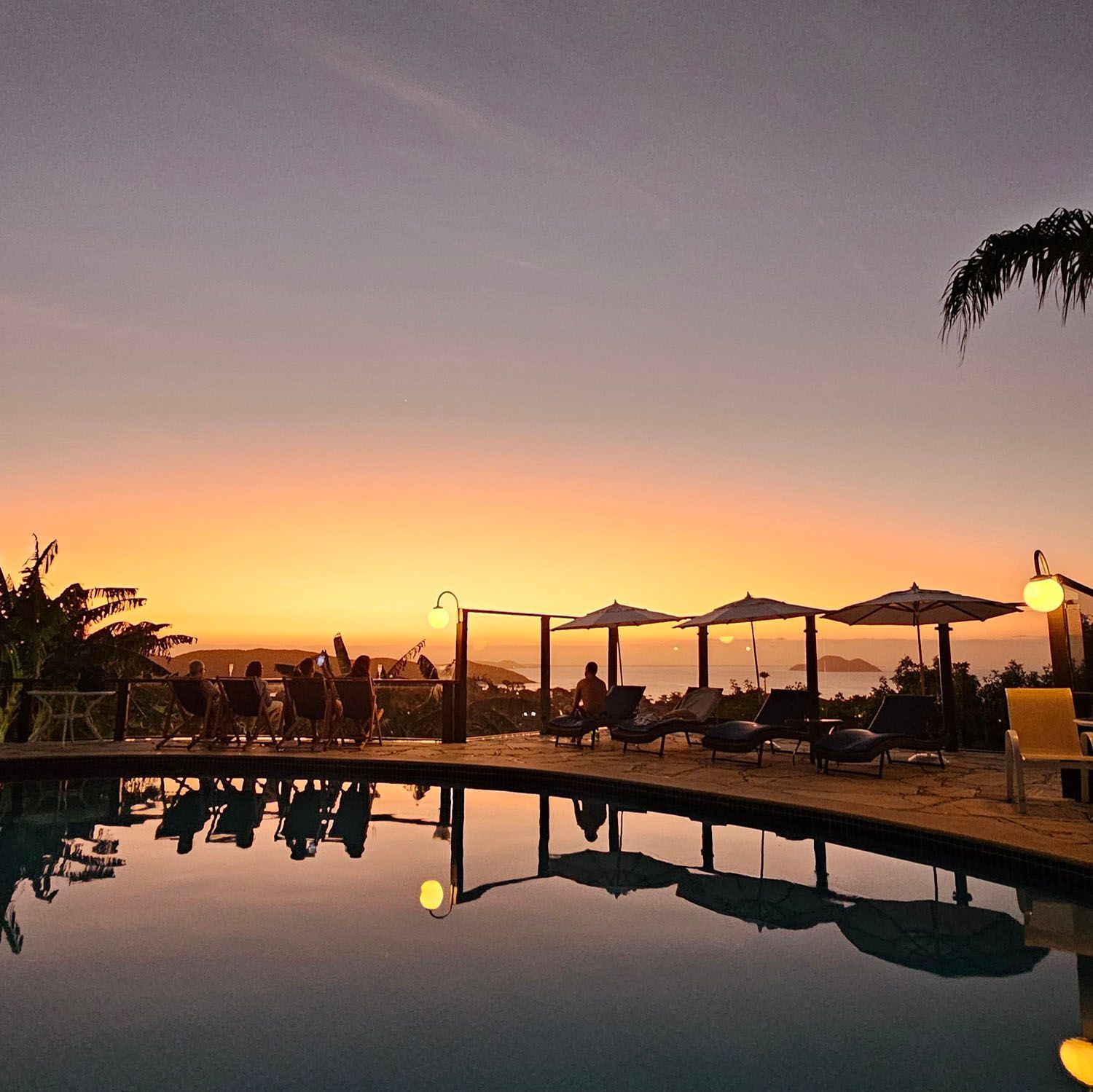 Um pôr do sol sobre uma piscina com cadeiras e guarda-sóis