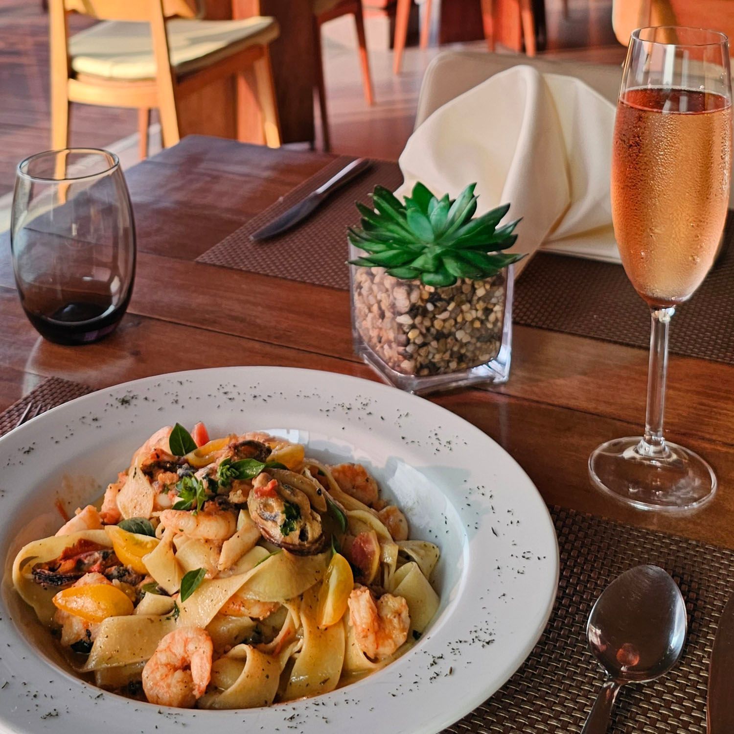 Um prato de macarrão com camarão fica em uma mesa ao lado de uma taça de vinho