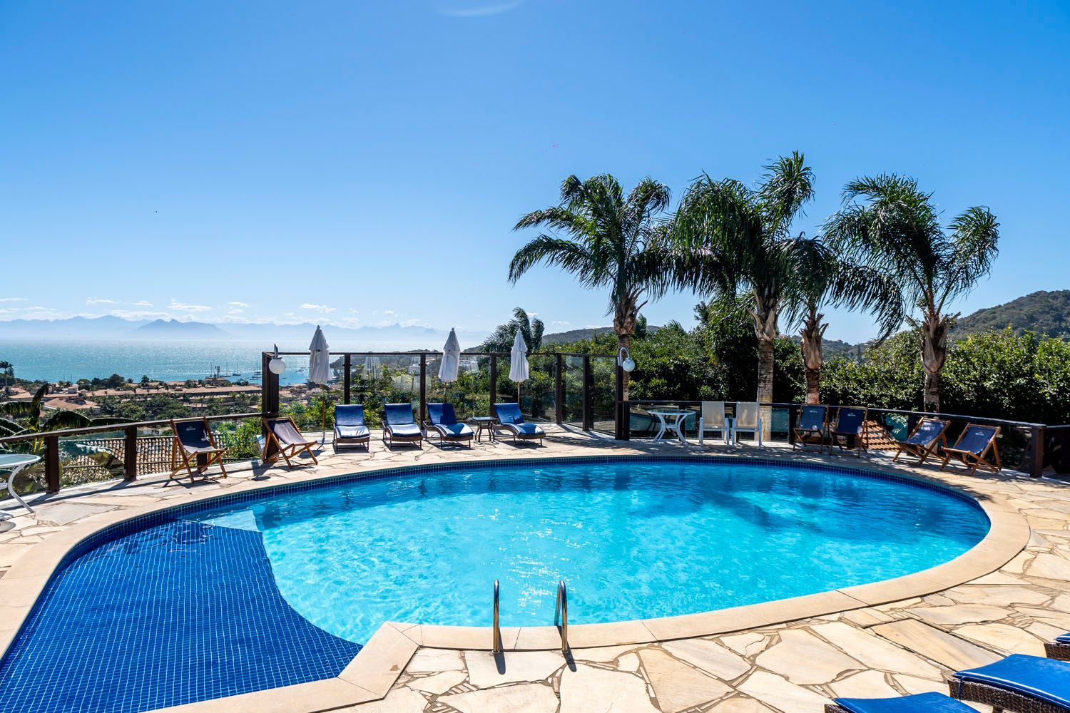 Uma grande piscina cercada por cadeiras e palmeiras em um dia ensolarado.