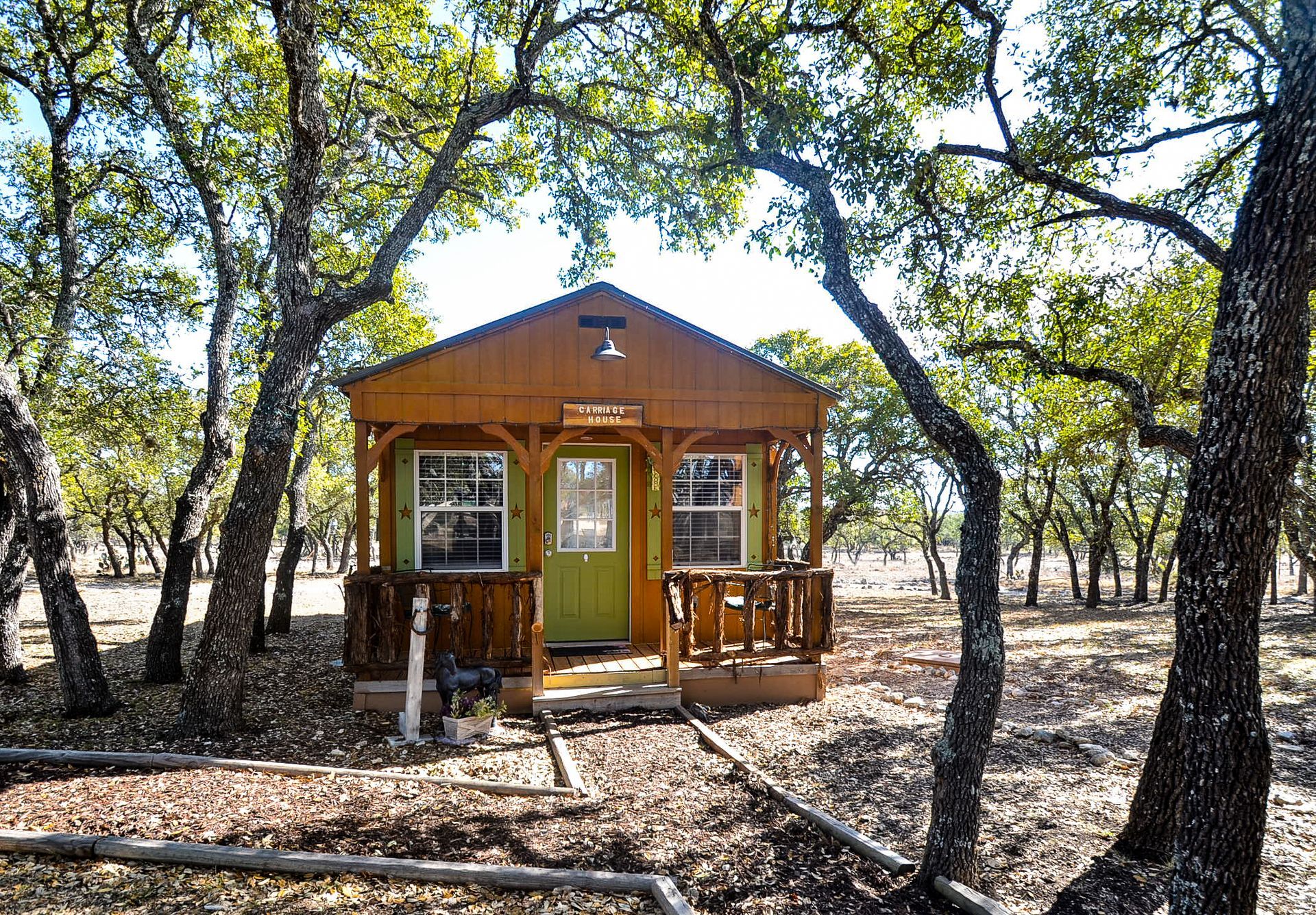 Small wooden cabin with a yellow door and porch, surrounded by trees in a wooded area.